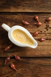 Tasty sauce in gravy boat, small onion bulbs and spice on wooden table, flat lay