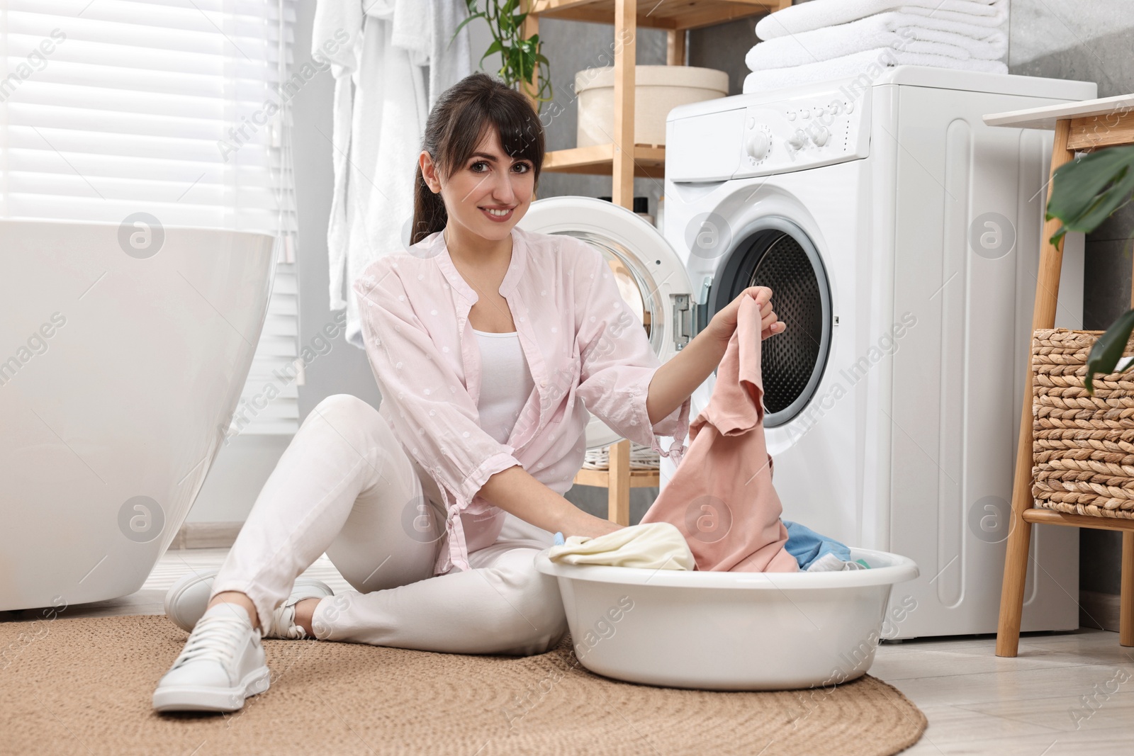 Photo of Happy young housewife with laundry near washing machine at home