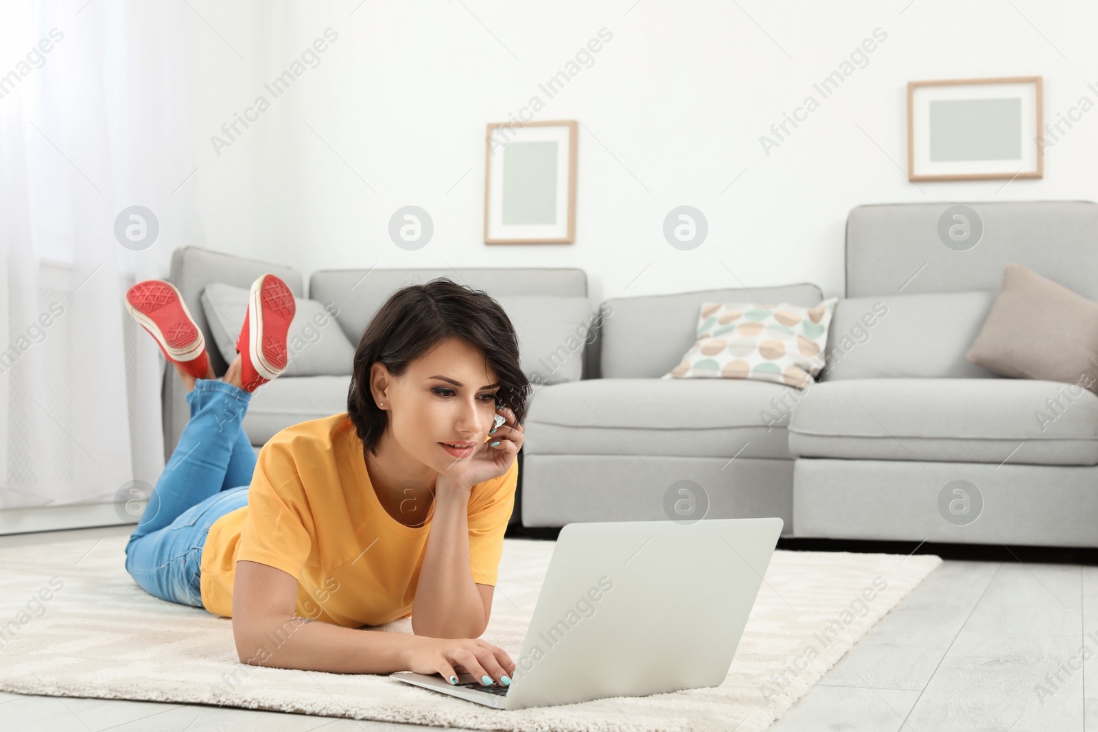 Photo of Young woman with modern laptop lying on floor at home