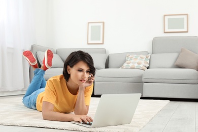 Photo of Young woman with modern laptop lying on floor at home