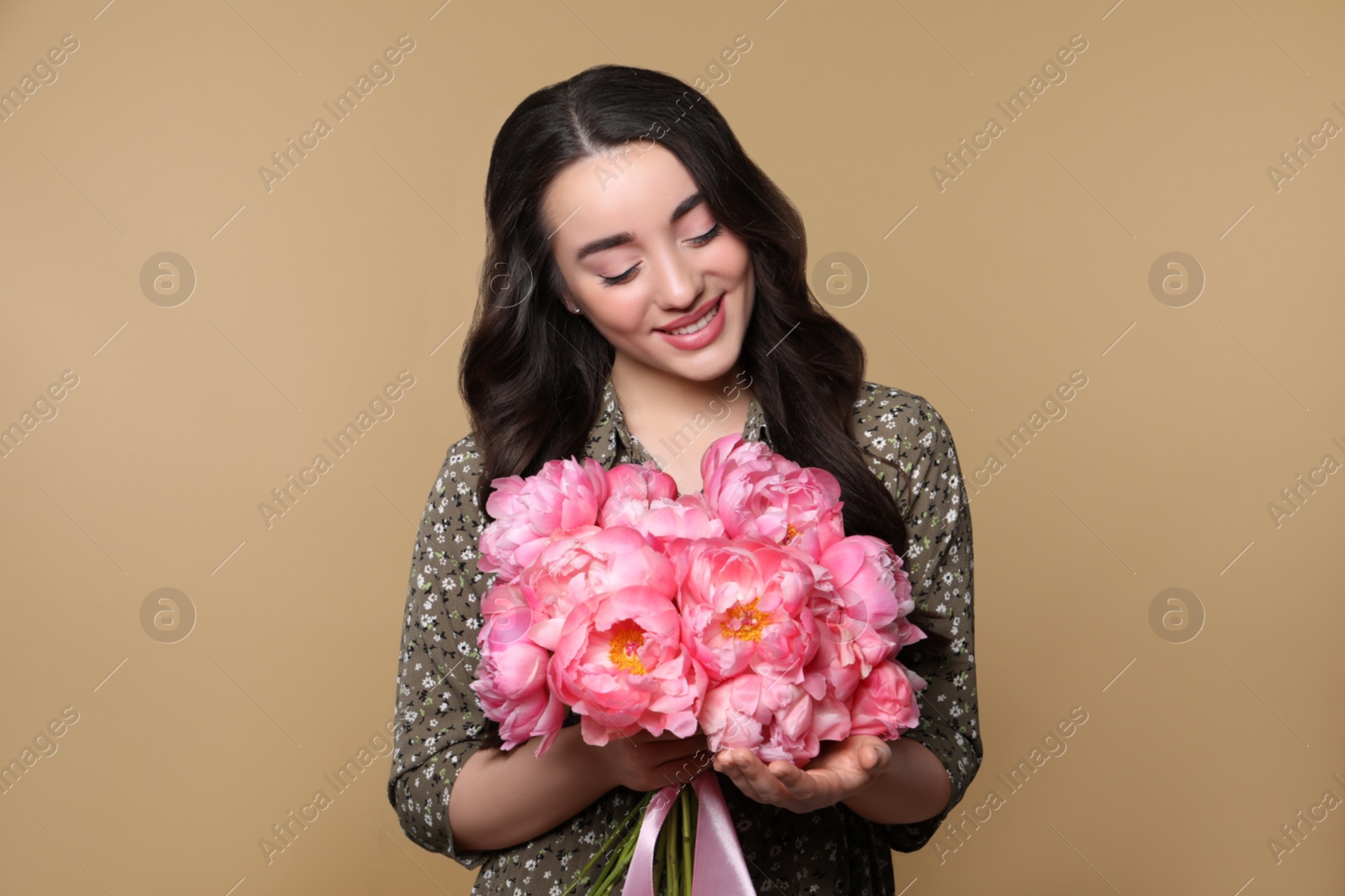 Photo of Beautiful young woman with bouquet of pink peonies on light brown background