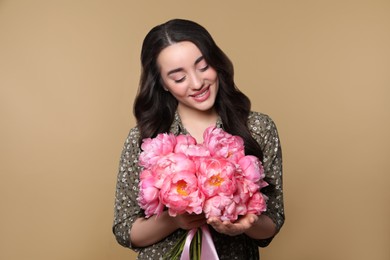 Beautiful young woman with bouquet of pink peonies on light brown background