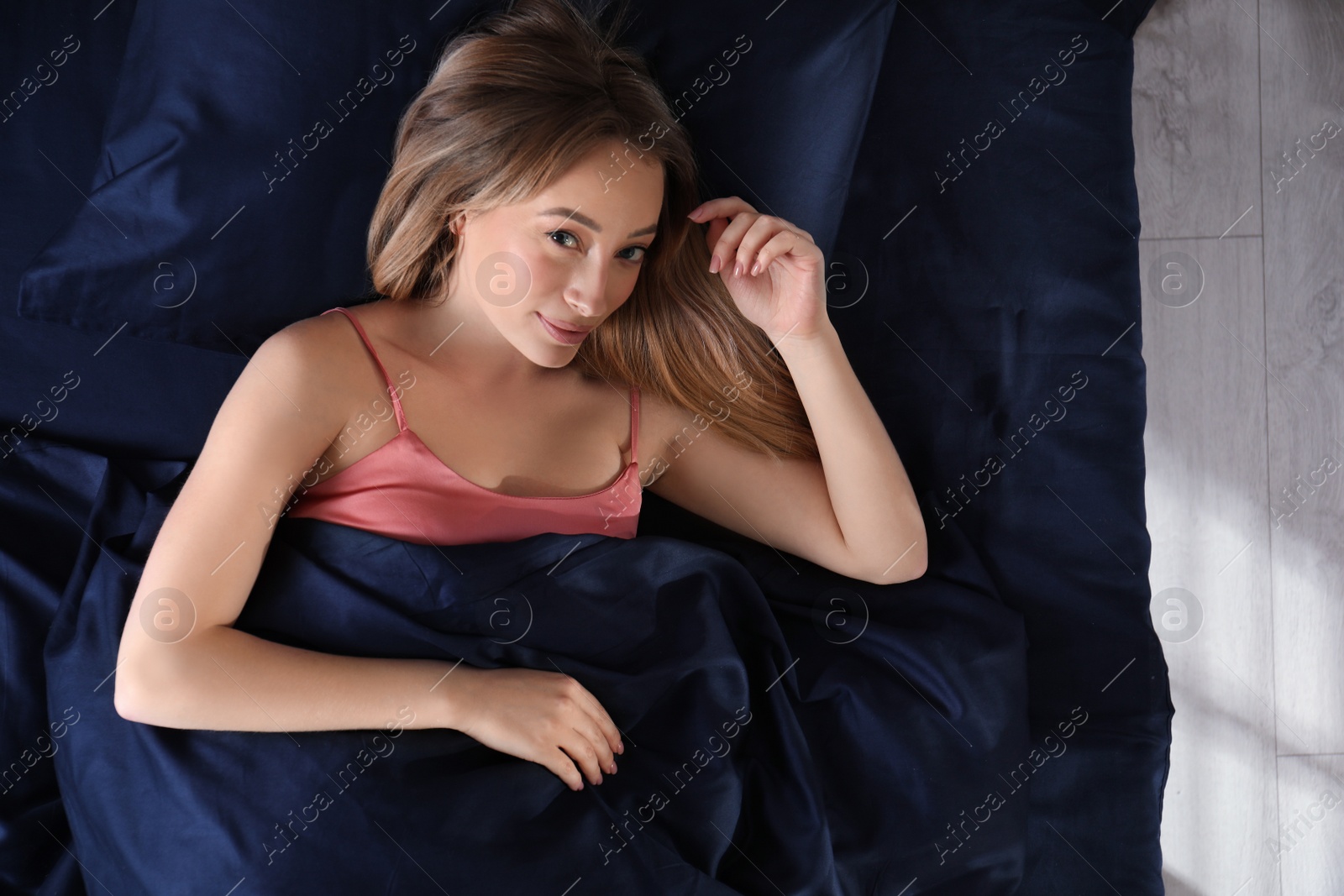 Photo of Young woman lying in comfortable bed with silky linens, top view