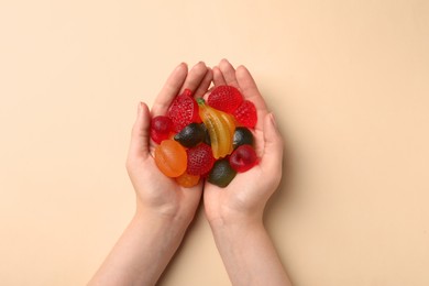 Woman holding pile of delicious fruit shaped gummy candies on beige background, top view