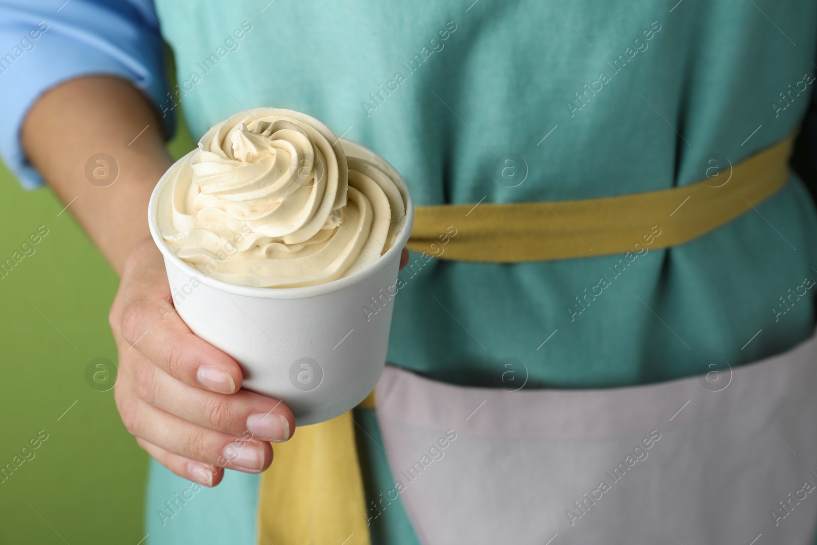 Photo of Woman holding cup with tasty frozen yogurt on green background, closeup