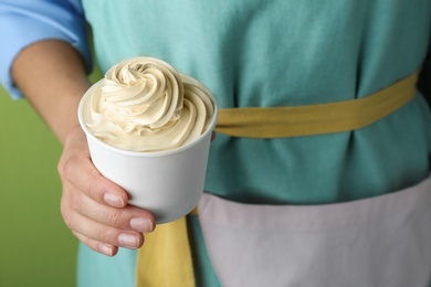 Woman holding cup with tasty frozen yogurt on green background, closeup