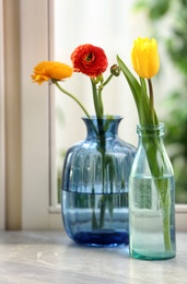 Photo of Different beautiful spring flowers in glassware on window sill