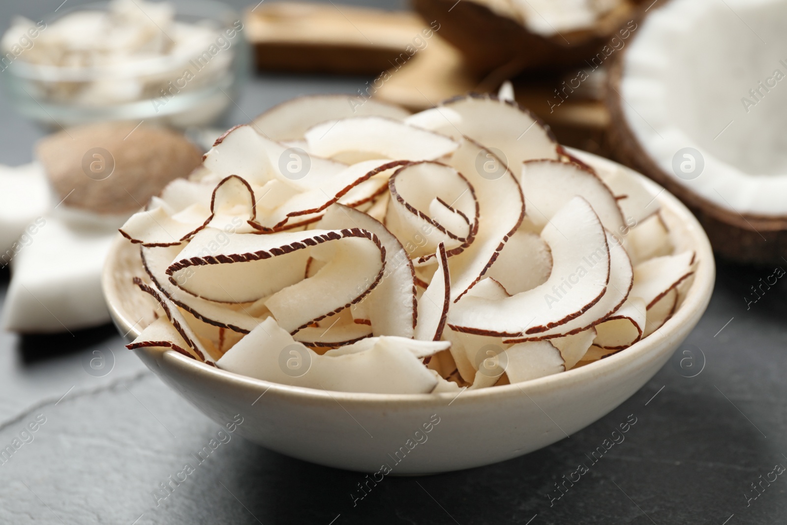 Photo of Tasty coconut chips in bowl on black table