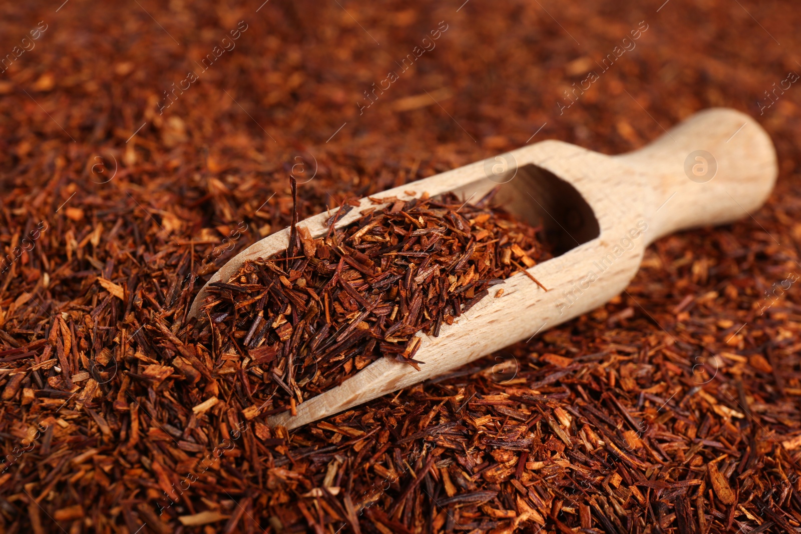 Photo of Heap of dry rooibos tea leaves with wooden scoop, closeup view