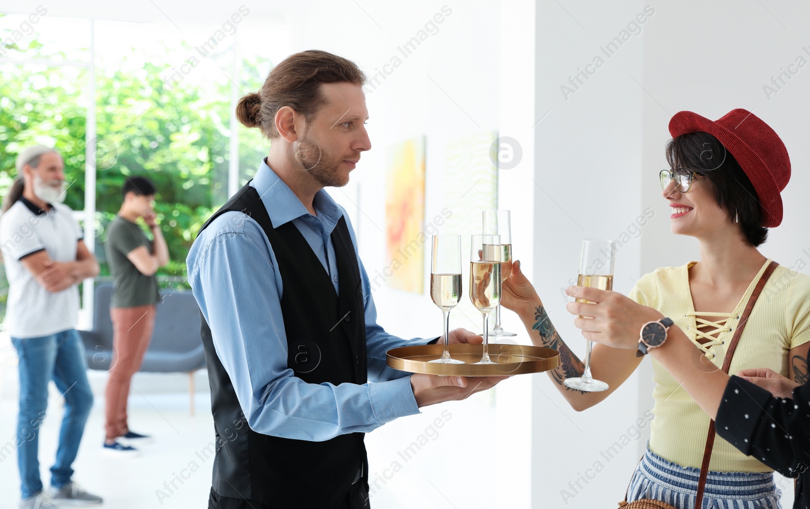 Photo of Waiter serving champagne to women at exhibition in art gallery