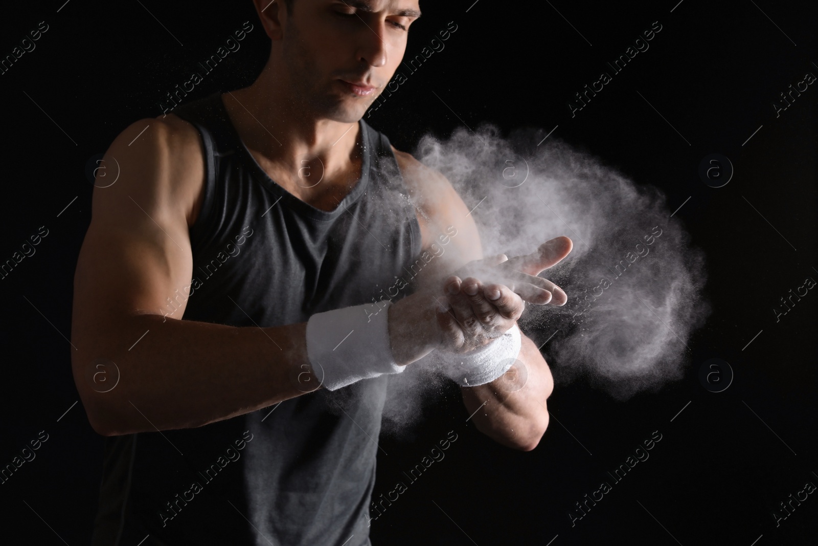 Photo of Young man applying chalk powder on hands against dark background