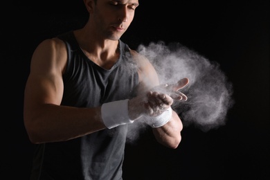 Photo of Young man applying chalk powder on hands against dark background