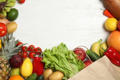 Frame of paper bag with fresh vegetables and fruits on white wooden background, top view. Space for text