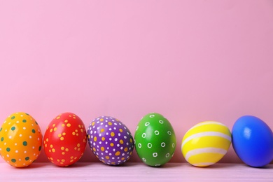 Photo of Decorated Easter eggs on table near color wall. Space for text