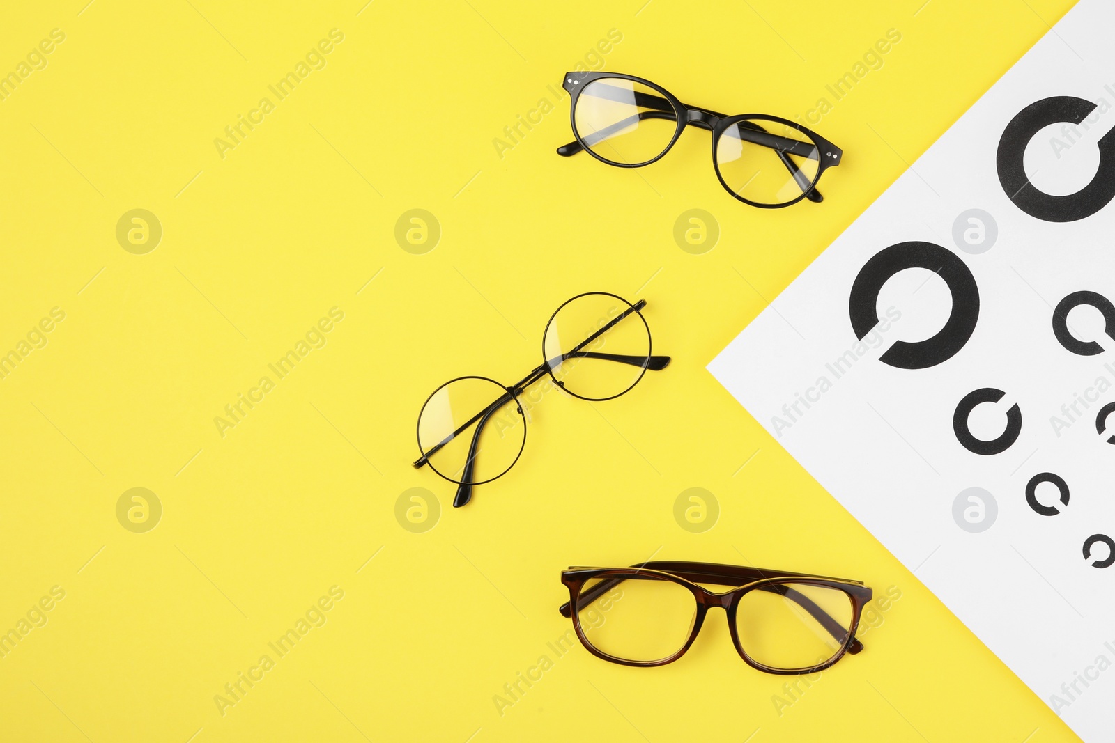 Photo of Vision test chart and glasses on yellow background, flat lay. Space for text