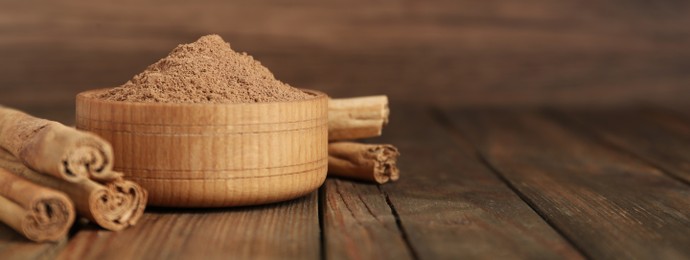 Cinnamon powder and sticks on wooden table, space for text. Banner design