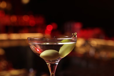 Photo of Martini glass with fresh cocktail and olives against blurred background, closeup. Space for text