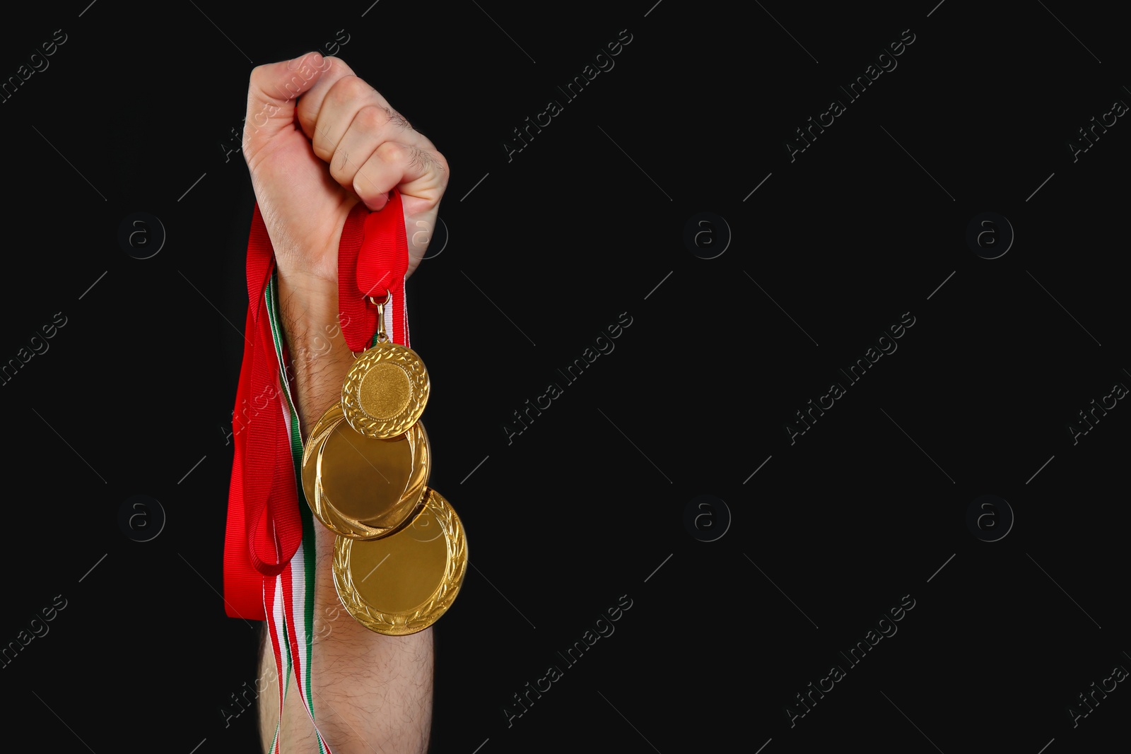 Photo of Man holding golden medals on black background, closeup. Space for design