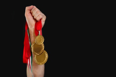 Man holding golden medals on black background, closeup. Space for design