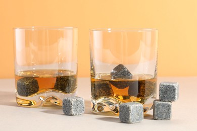 Photo of Whiskey stones and drink in glasses on light table, closeup