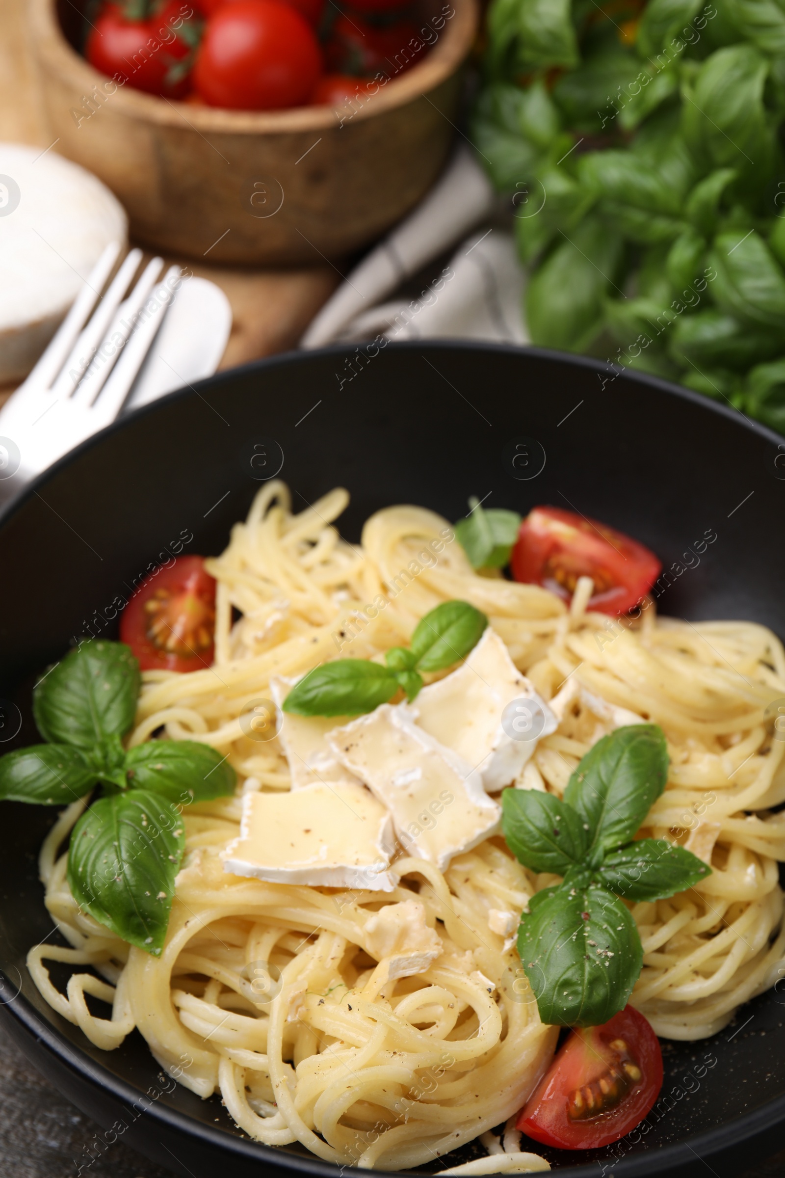 Photo of Delicious pasta with brie cheese, tomatoes and basil leaves in bowl, closeup