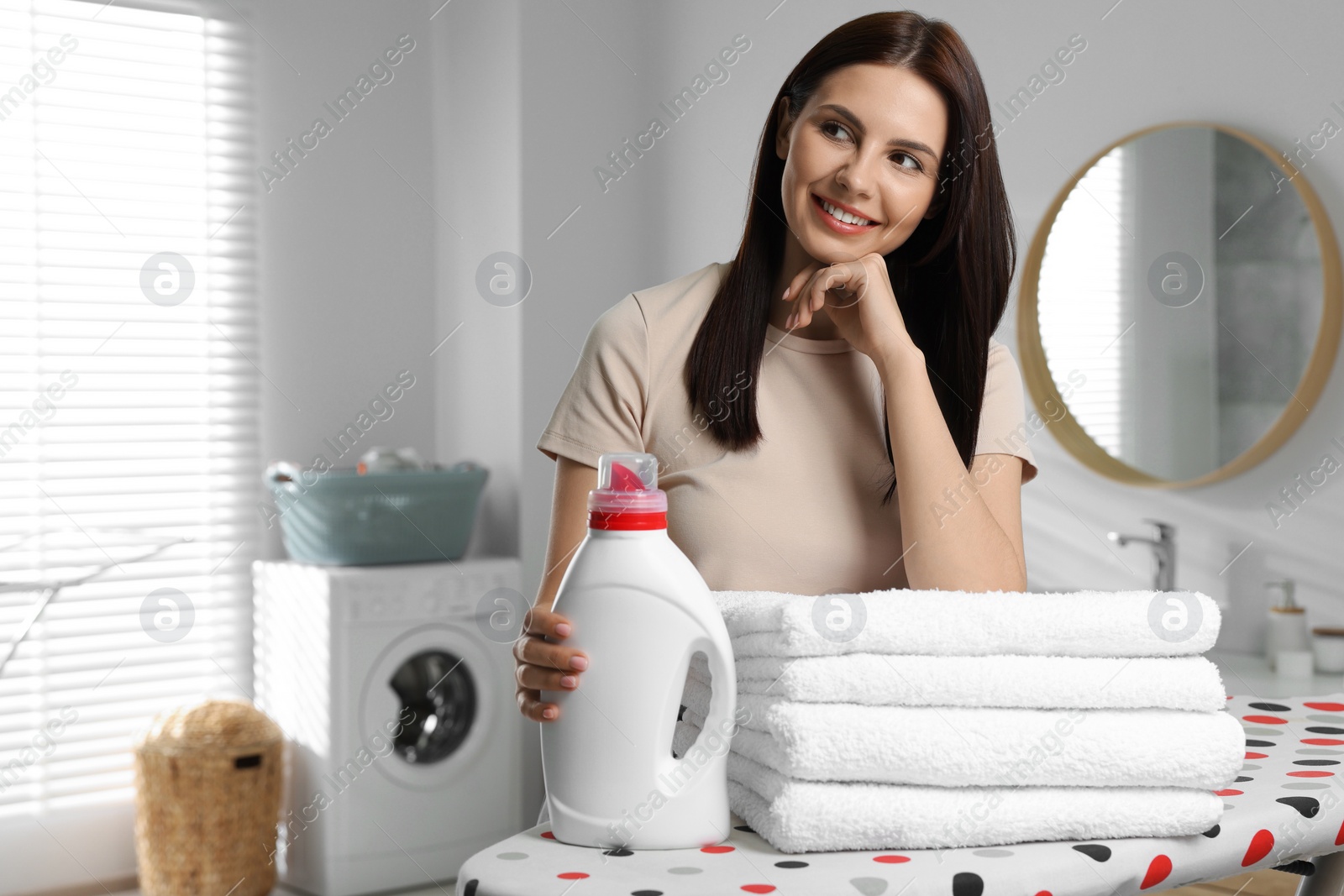 Photo of Woman near fabric softener and clean towels in bathroom, space for text