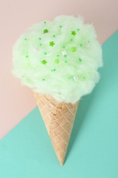 Sweet cotton candy in waffle cone on color background, top view