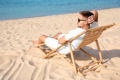 Young man relaxing in deck chair on sandy beach