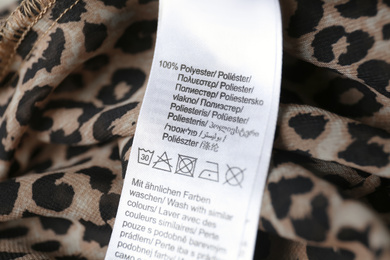 Photo of Clothing label with care symbols and material content on polyester shirt, closeup view. Wash with similar colors