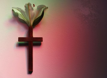 Photo of Wooden cross and lily flower on textured table in color lights, top view with space for text. Religion of Christianity