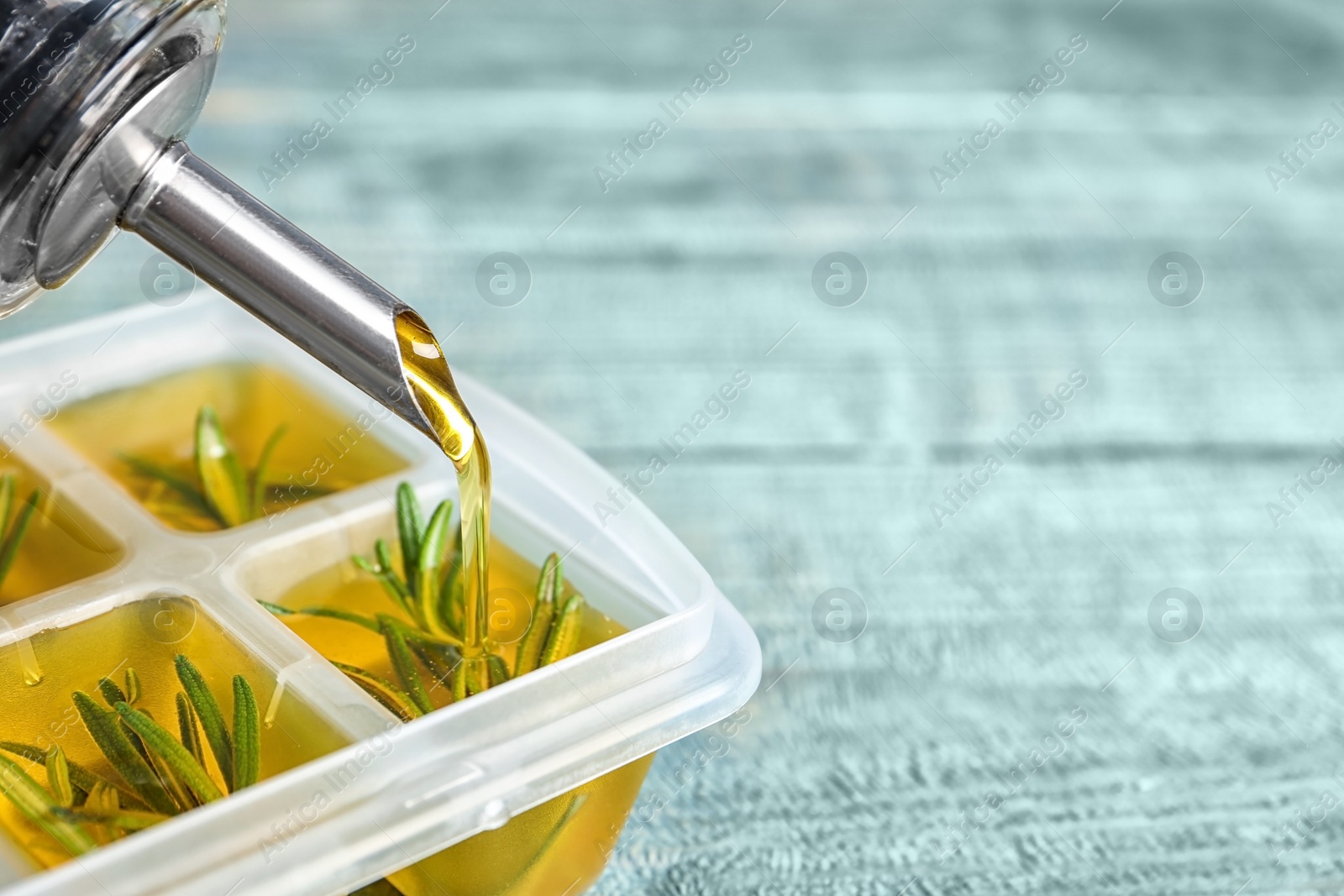 Photo of Pouring olive oil into ice cube tray with rosemary on table, closeup. Space for text