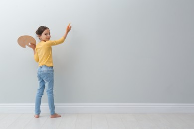 Photo of Little girl painting on light grey wall indoors. Space for text