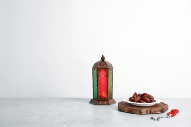 Photo of Muslim lantern Fanous, dried dates and prayer beads on table against light background