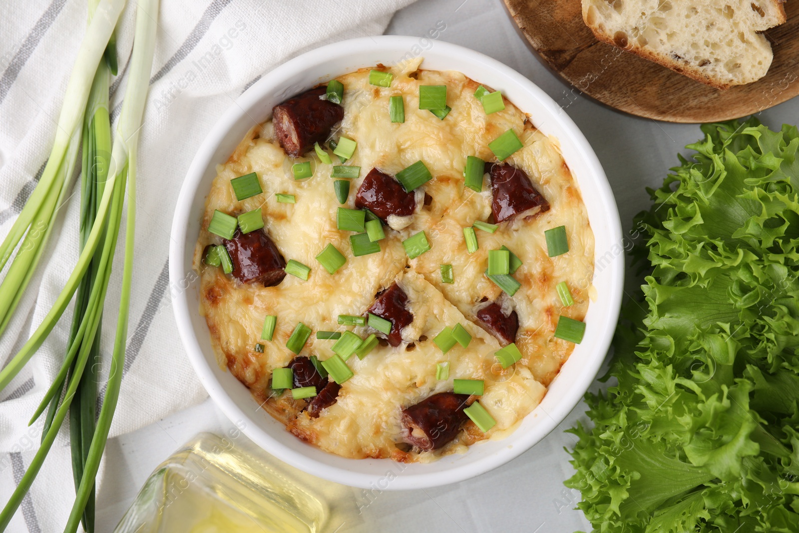 Photo of Tasty sausage casserole in baking dish served on white tiled table, flat lay