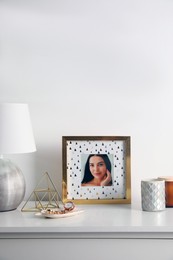 Photo frame with portrait of beautiful young woman near stylish decor on white table