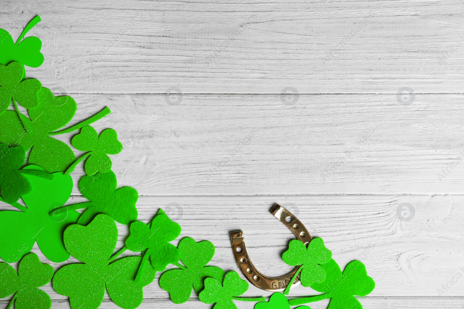 Photo of Flat lay composition with clover leaves and horseshoe on white wooden background, space for text. St. Patrick's day