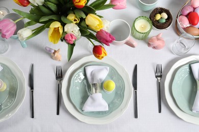 Photo of Easter celebration. Festive table setting with beautiful flowers and painted eggs, flat lay