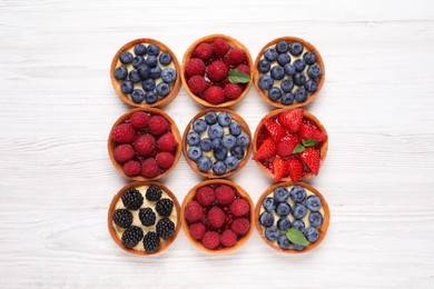 Photo of Tartlets with different fresh berries on white wooden table, flat lay. Delicious dessert