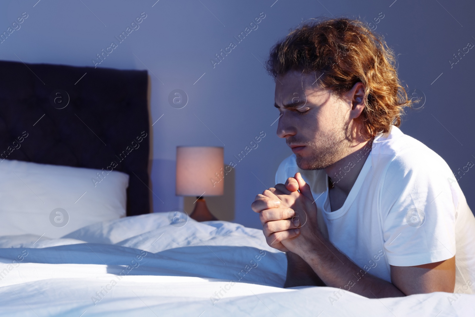 Photo of Handsome young man saying bedtime prayer in dark room at night