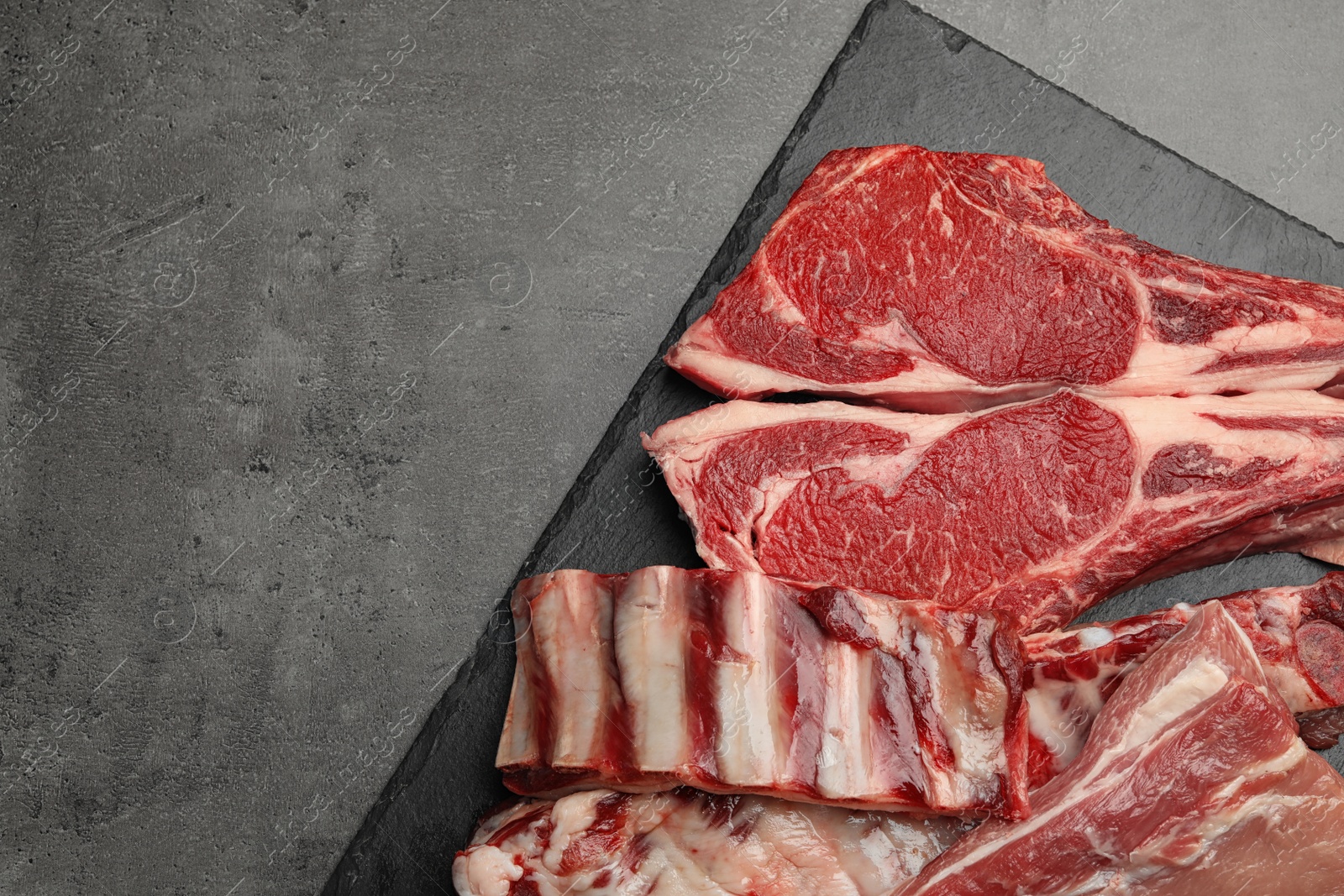 Photo of Slate plate with raw meat on grey table, flat lay. Space for text