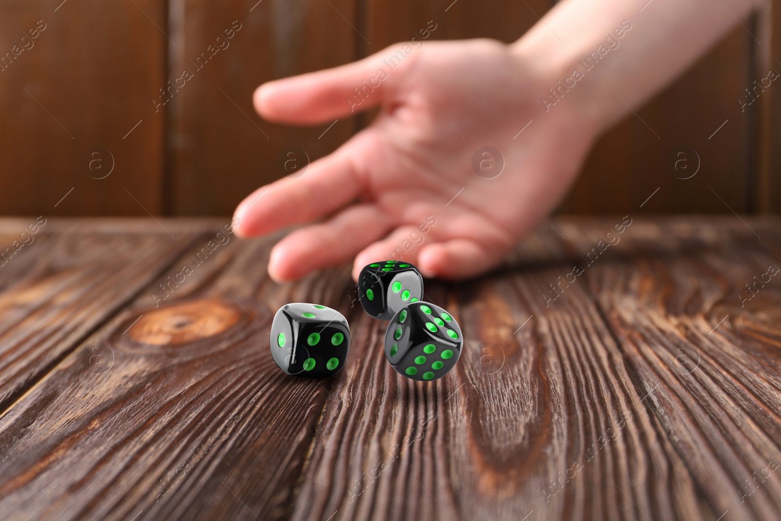 Image of Woman throwing black dice on wooden table, closeup