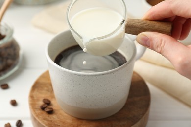 Photo of Woman pouring milk into cup with coffee at white table, closeup