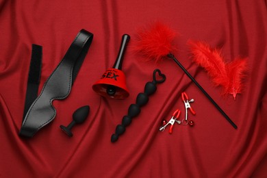 Photo of Sex toys and accessories on red fabric, flat lay