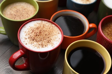 Photo of Many different cups with aromatic hot coffee on wooden table, closeup