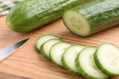 Photo of Fresh cucumbers and knife on wooden cutting board, closeup