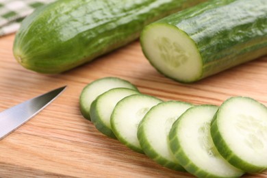 Fresh cucumbers and knife on wooden cutting board, closeup