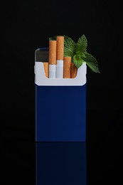 Photo of Pack of menthol cigarettes and mint on black background