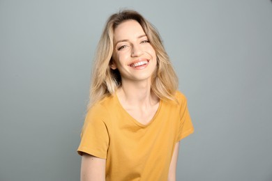 Portrait of happy young woman with beautiful blonde hair and charming smile on grey background