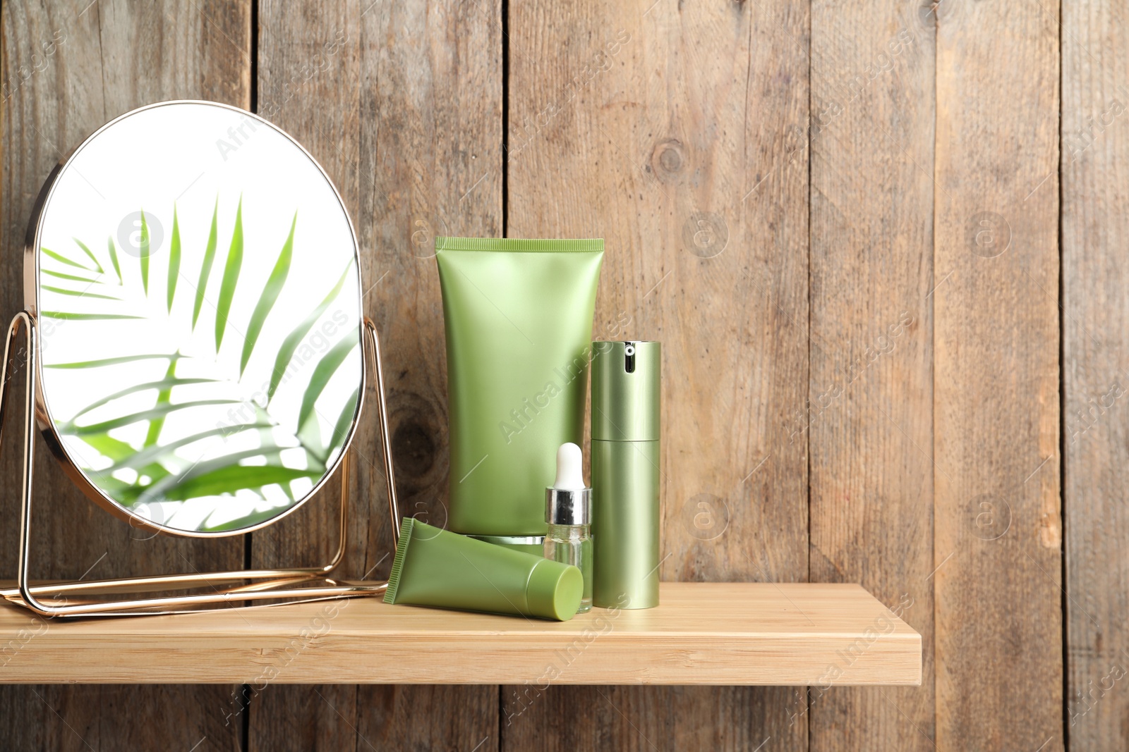 Photo of Set of cosmetic products and mirror on shelf near wooden wall