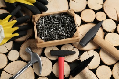 Photo of Hammers, gloves and metal nails on stumps, flat lay